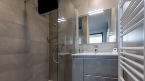 Ein modernes Badezimmer mit einer in Glas eingefassten Dusche, einem großen Spiegel und einer integrierten Toilette.