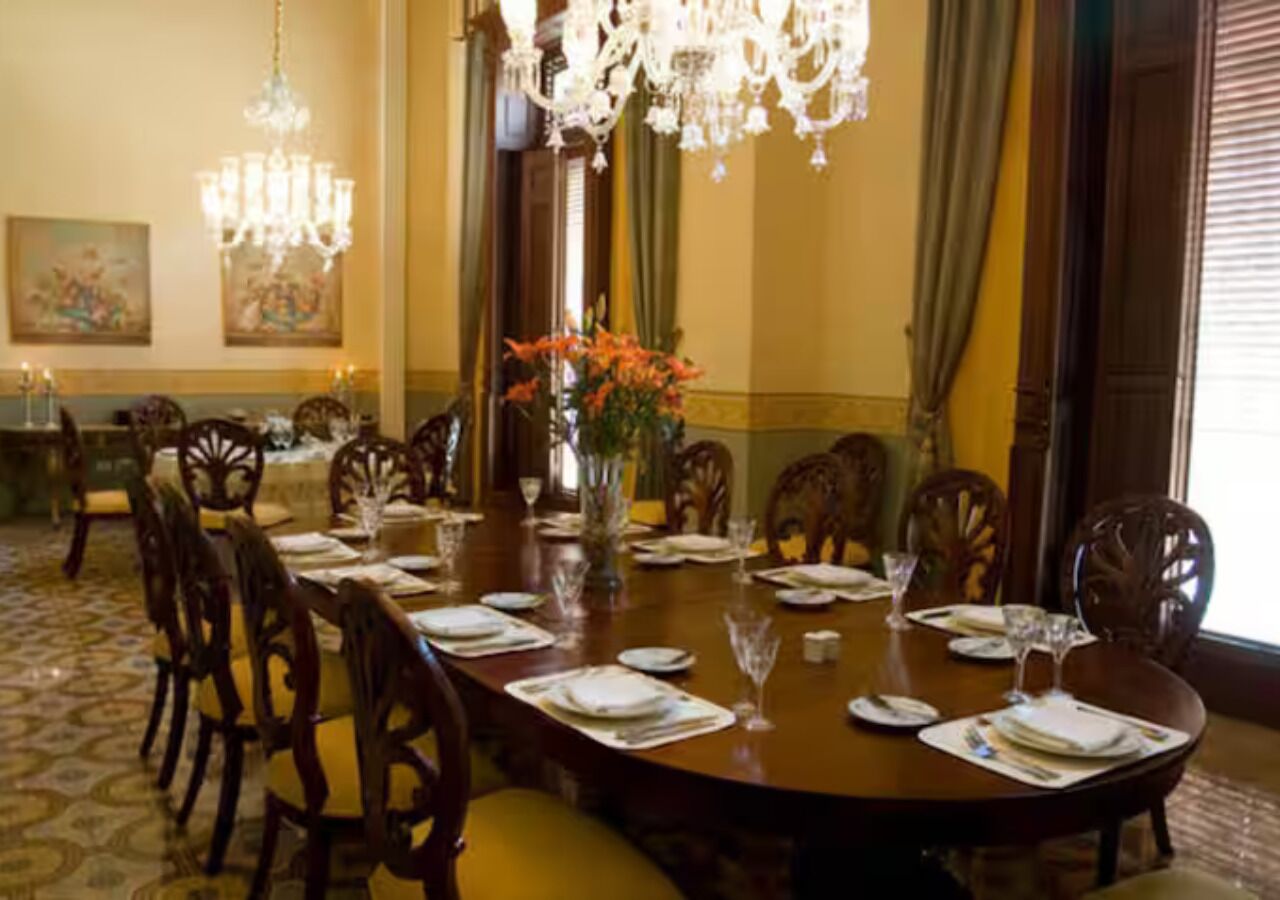 A formal dining room with a round table set for six, surrounded by wooden chairs.