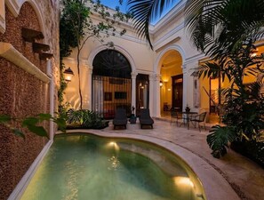 Une cour avec une piscine, des espaces aménagés pour s’asseoir et un bâtiment orné d’arches et de colonnes.