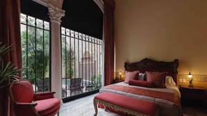 A bedroom with a large bed, a red armchair, and a view of a balcony with plants. - La Casa del Centro, Mérida by Cercana  (Mérida)