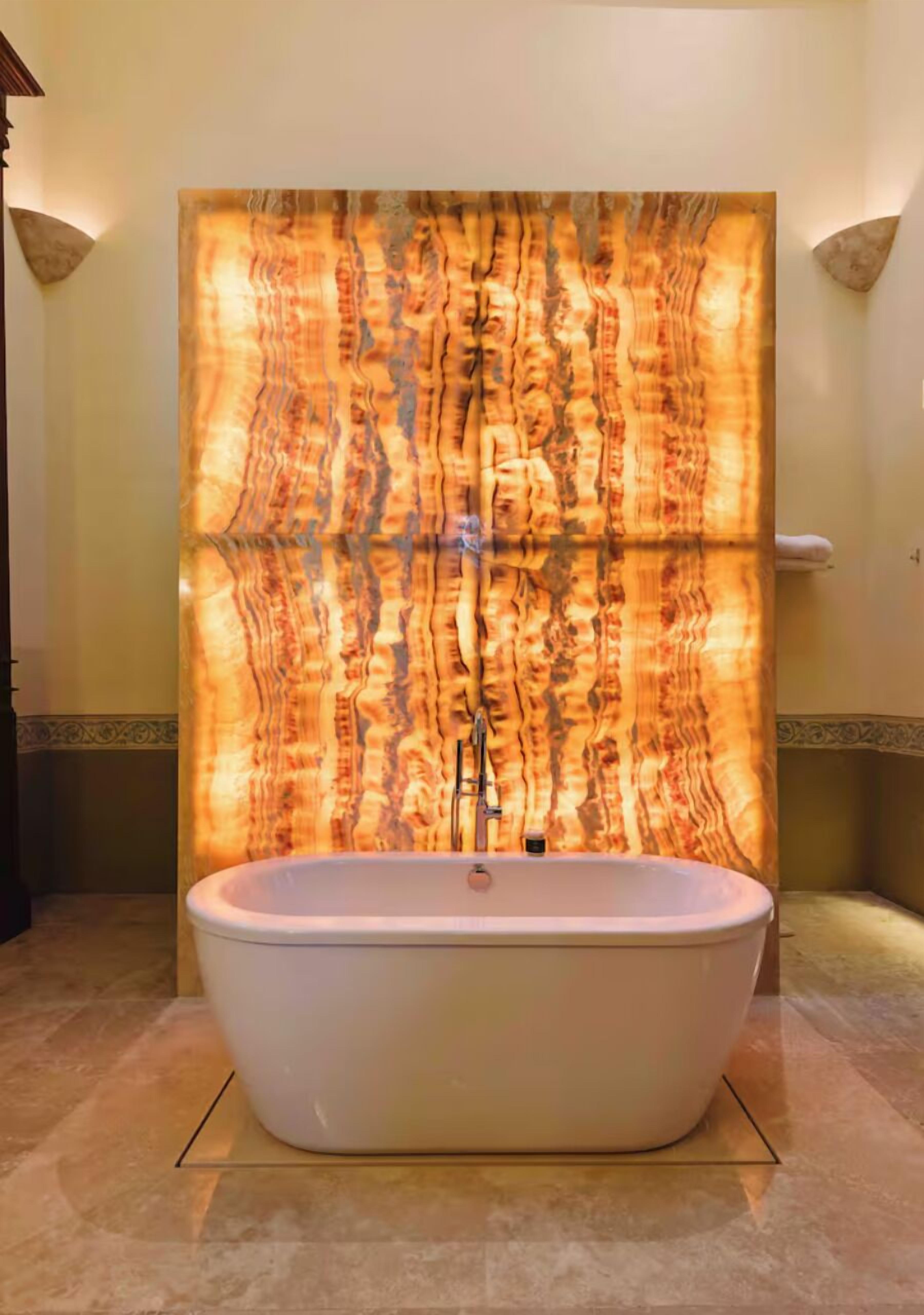 A freestanding bathtub in a bathroom with a large, textured wall behind it.