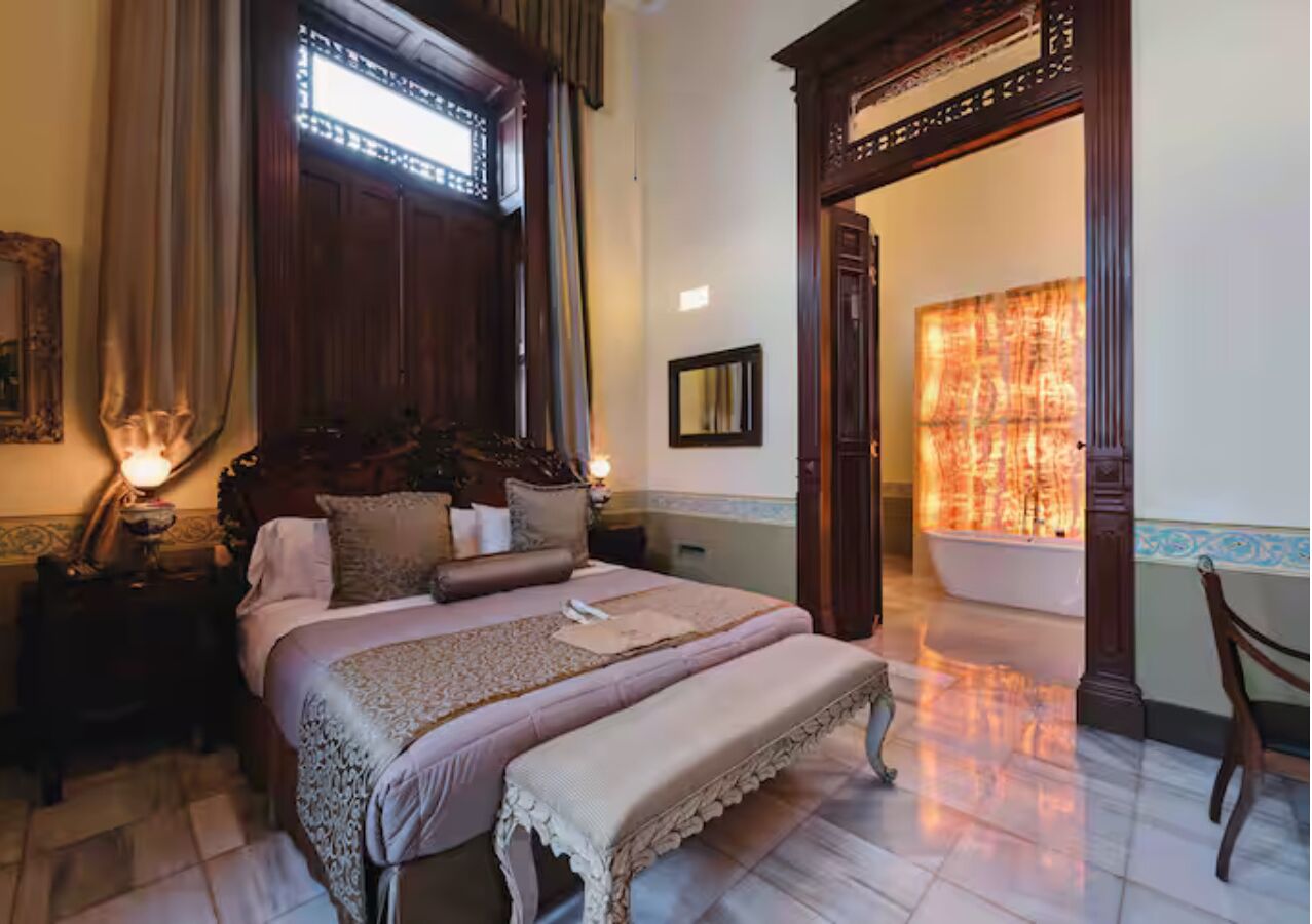 Une chambre à coucher de style traditionnel, avec un grand lit, une table de chevet, un miroir et une vue sur une salle de bain dotée d’une baignoire.