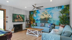 A living room with a pool table, a sofa, a fireplace, and a mural of a pirate ship. - Pirates Cove: Heated Pool, Arcades, Playground and more! (Garden Grove)