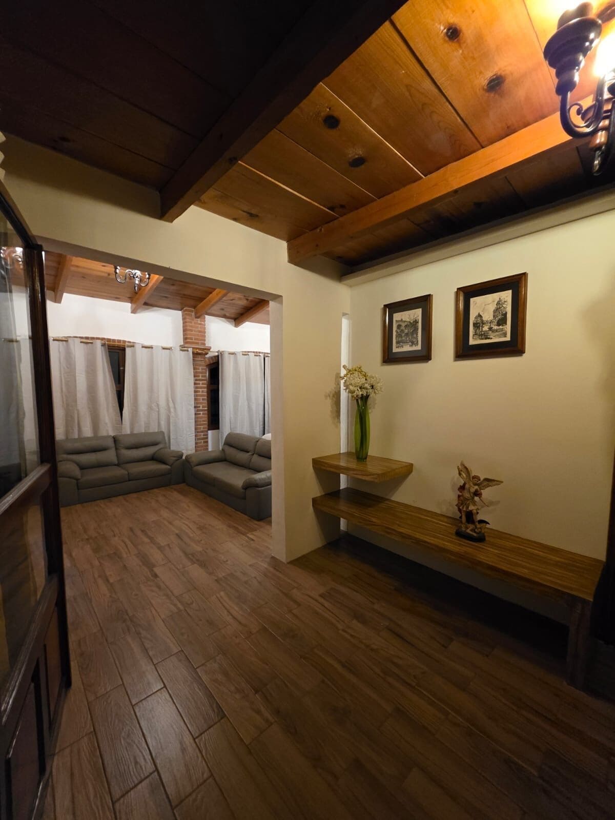 A room with a wooden floor, a sofa, a bench, and a wall with framed pictures.