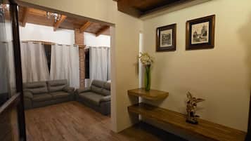 A room with a wooden floor, a sofa, a bench, and a wall with framed pictures.