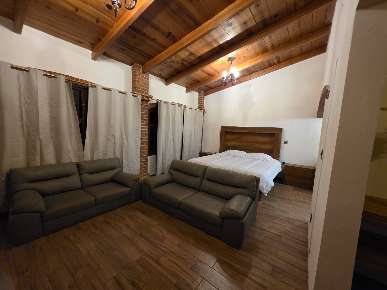 Una stanza con soffitto in legno, un letto, due divani e un muro in mattoni.