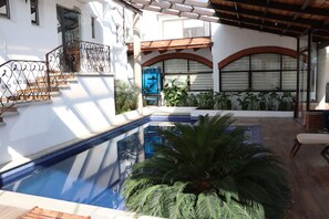 A swimming pool with a wooden deck, surrounded by potted plants and a covered patio area. - Hotel Cuamanco (Huamantla)