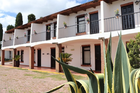 A two-story building with a white facade, black window frames, and a balcony with potted plants. - Hotel Cuamanco (Huamantla)