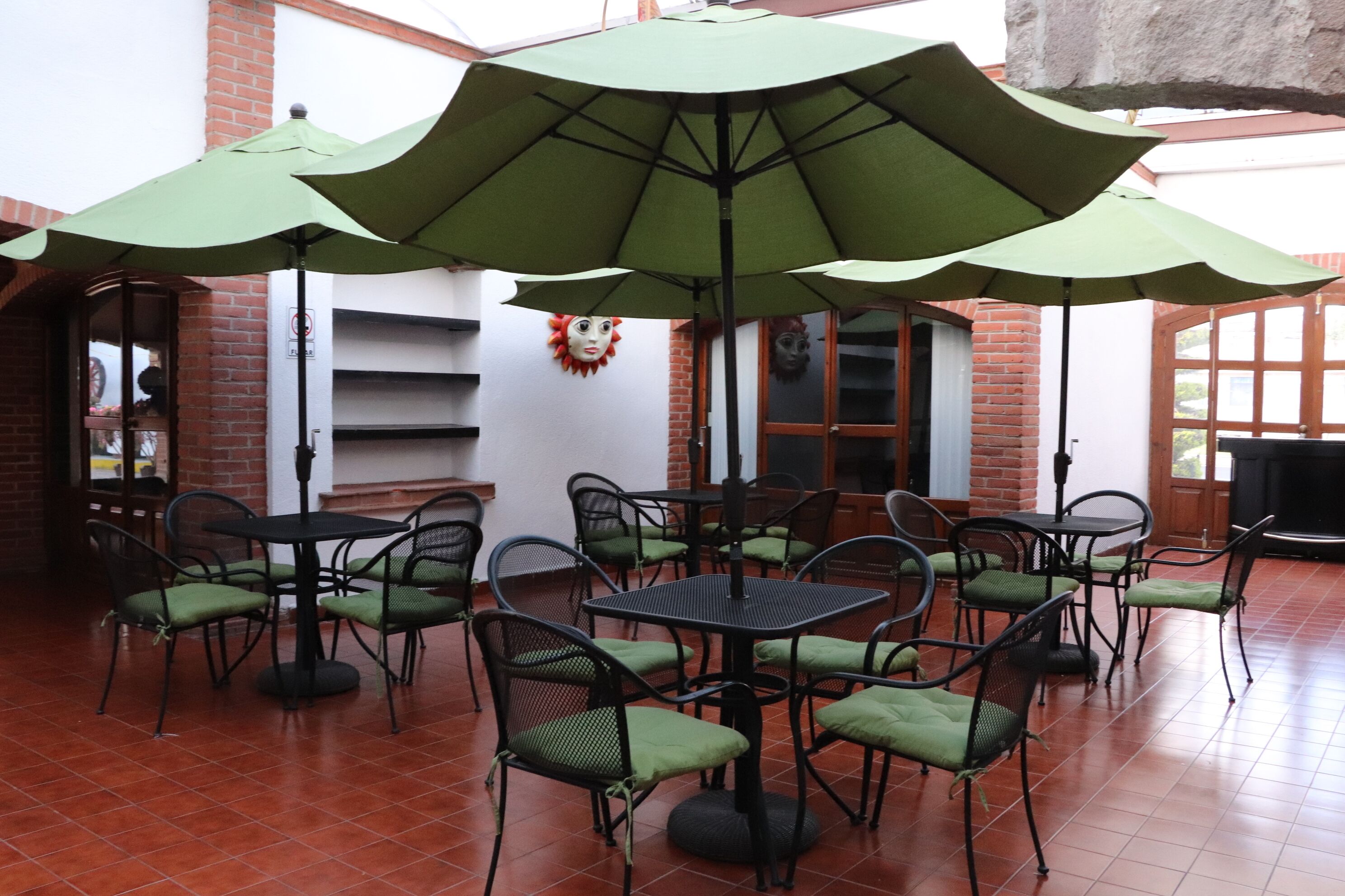 Un patio con mesas y sillas, sombrillas verdes y una pared de ladrillo.