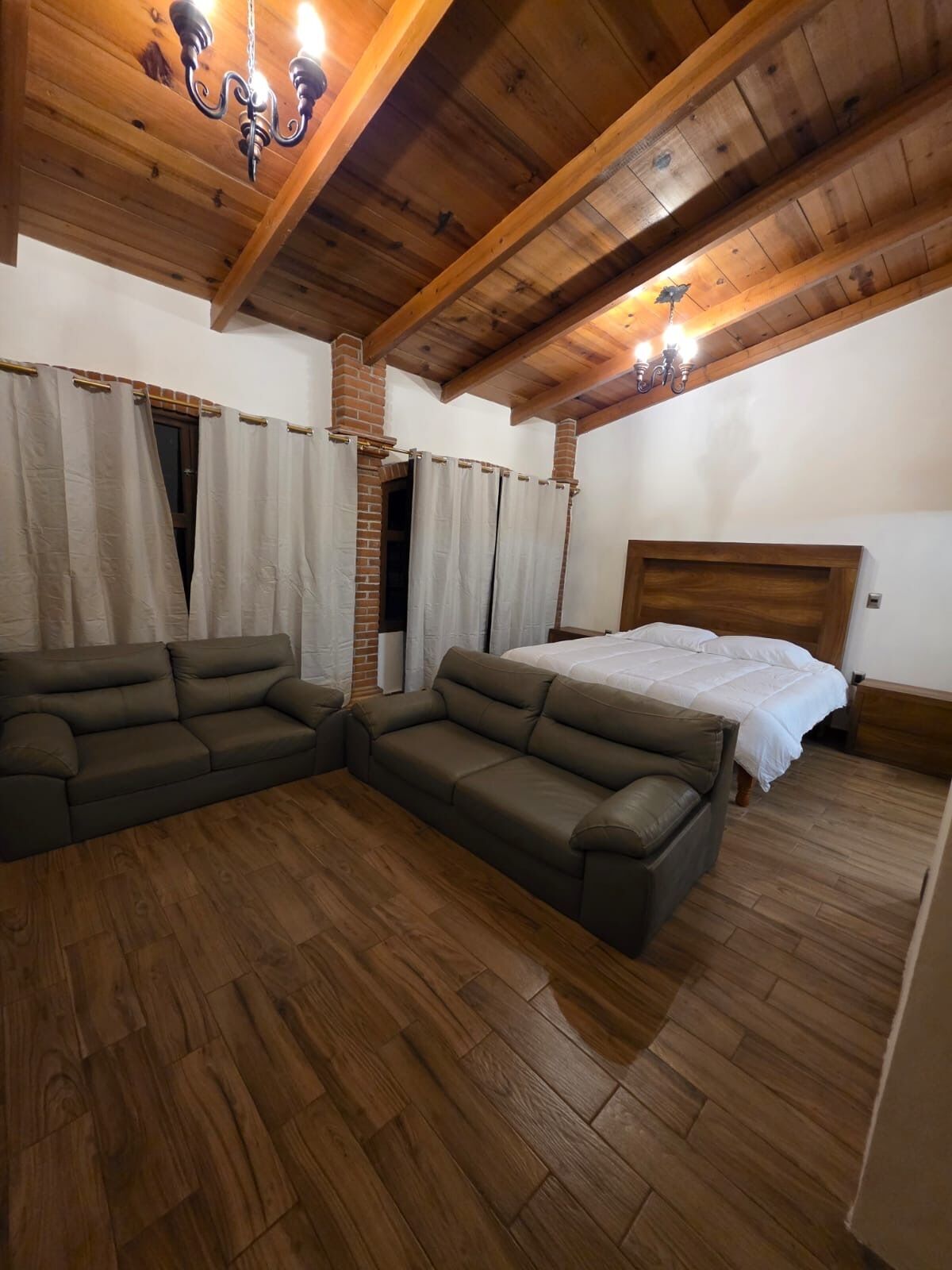 A bedroom with a wooden ceiling, a bed, a sofa, and a shower area.