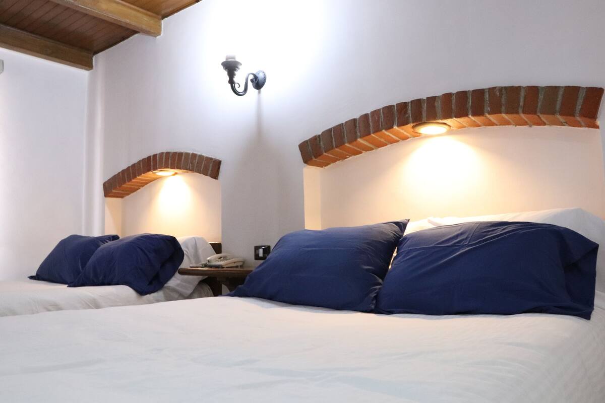 Une chambre d’hôtel avec deux lits, chacun agrémenté de draps bleus et blancs, un arc en briques et un luminaire fixé au mur.