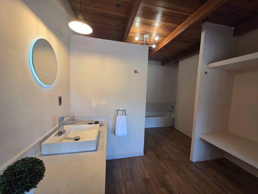 Une salle de bain moderne avec un plafond en bois, un miroir rond, un lavabo blanc et une baignoire.