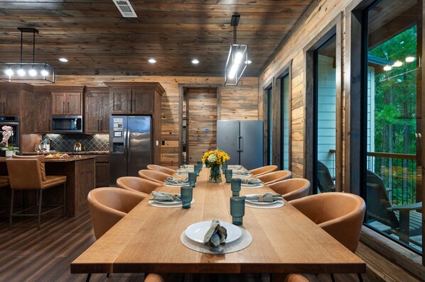 A modern kitchen with stainless steel appliances, a wooden dining table set for six, and large windows offering a view of the outdoors.