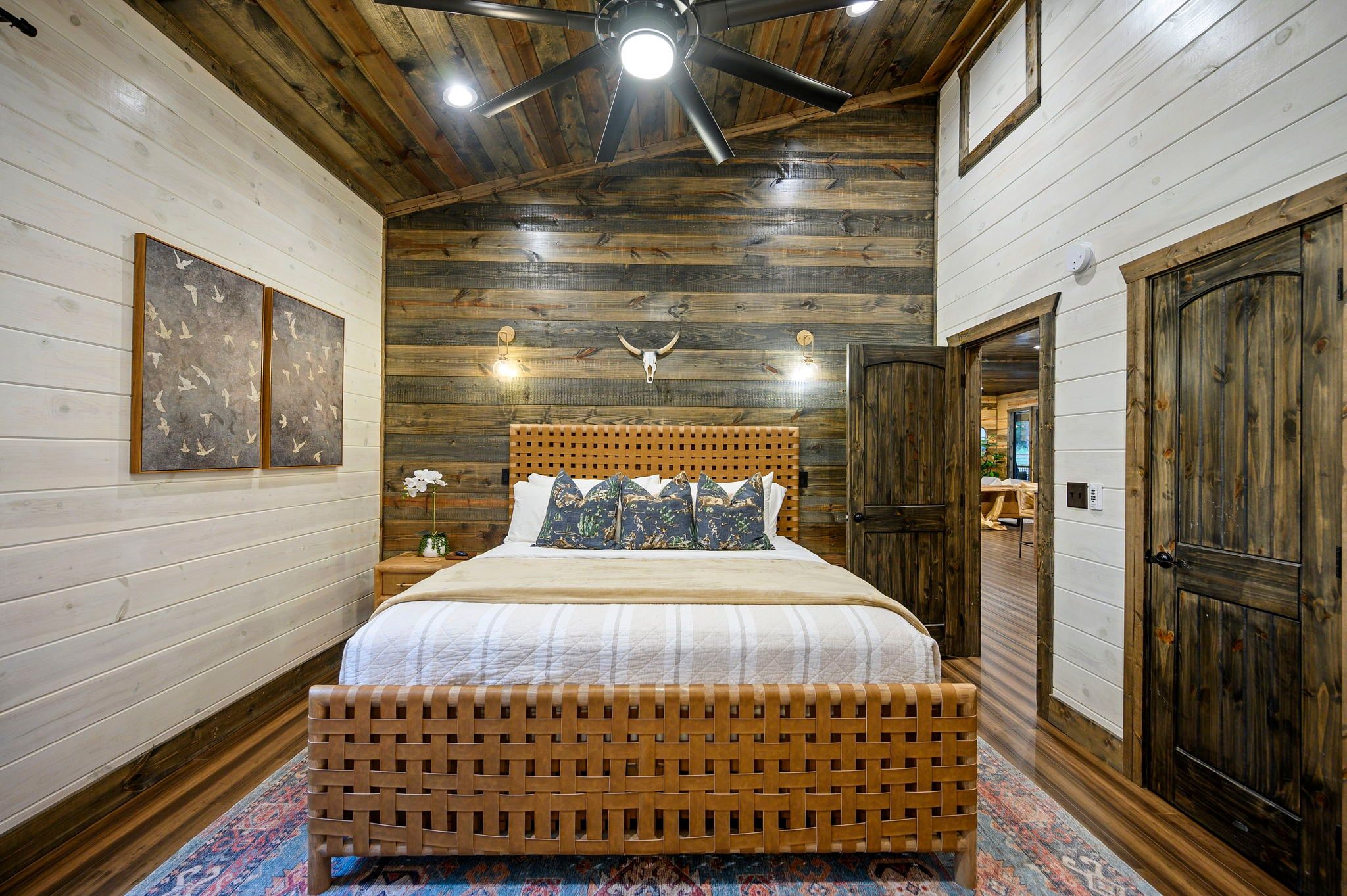 A room with a bed, wooden walls, a ceiling fan, and a door.
