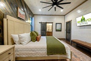 A bedroom with a bed, a nightstand, a bench, a ceiling fan, and a bathroom visible through an open door. - 8 Bedroom W/Pool, Playset, Putt-Putt, Game Room, ATV Access (Broken Bow)