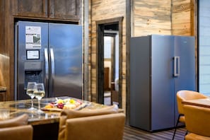 A modern kitchen with stainless steel appliances, a water dispenser, and a dining area with a table set for two. - 8 Bedroom W/Pool, Playset, Putt-Putt, Game Room, ATV Access (Broken Bow)