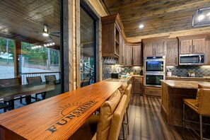 Un restaurant doté d’un bar en bois et d’un espace salon, d’une cuisine équipée d’appareils en acier inoxydable et de grandes fenêtres donnant sur une zone recouverte de gravier.
