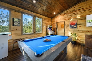 A pool table in a cabin with wooden walls and windows overlooking a forest. - 8 Bedroom W/Pool, Playset, Putt-Putt, Game Room, ATV Access (Broken Bow)