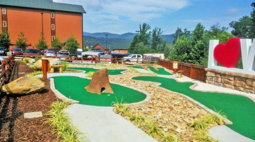 A miniature golf course with a green putting area, a rock feature, and a large heart-shaped sign.