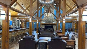 A spacious indoor area with wooden beams, a stone fireplace, leather seating, and a bar area. - Smoky Mountain Resort Luxury Cabin (Gatlinburg)