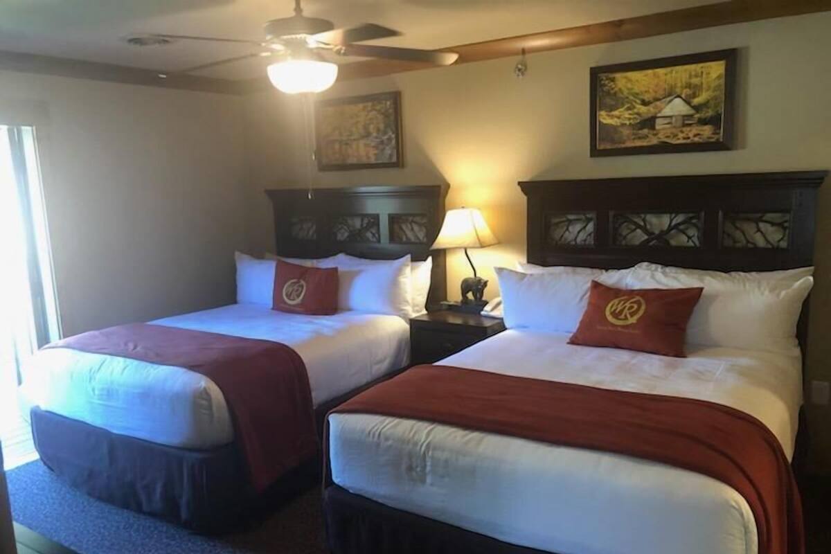 A hotel room with two beds, a ceiling fan, a nightstand with a lamp, and artwork on the walls.