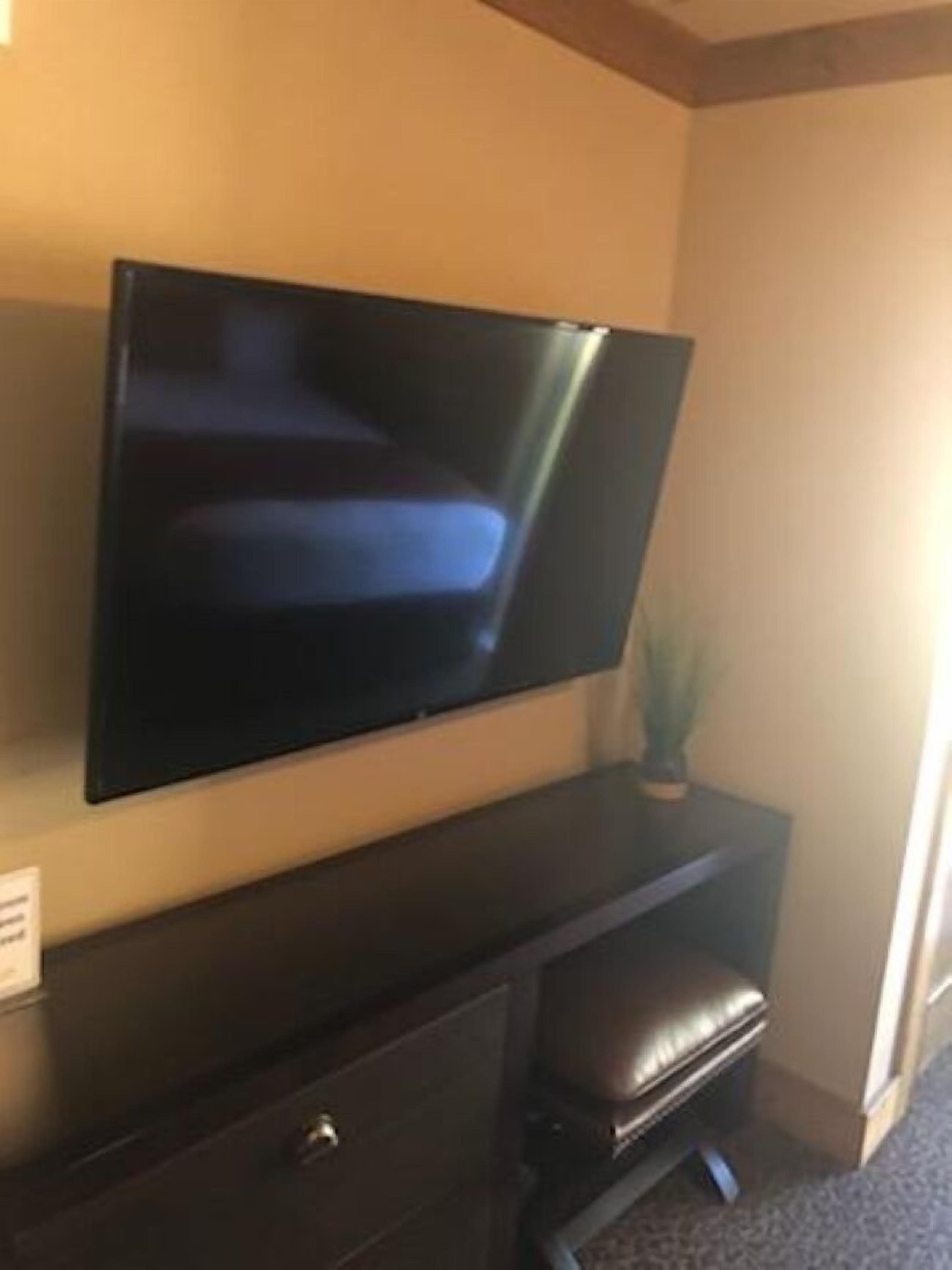 Ein Flachbildfernseher ist an einem dunklen Holzschrank befestigt, daneben befindet sich eine kleine Bank und ein Blumentopf.