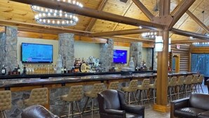 A bar area with stone walls, multiple televisions, and bar stools. - Smoky Mountain Resort Luxury Cabin (Gatlinburg)