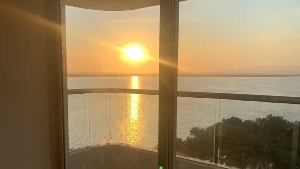 En balkon med glasdør og udsigt til solnedgangen over vandet.