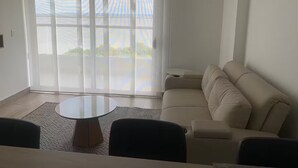 En moderne stue med en beige sofa, et rundt sofabord og en stor skydedør med udsigt til grøn vegetation udenfor.