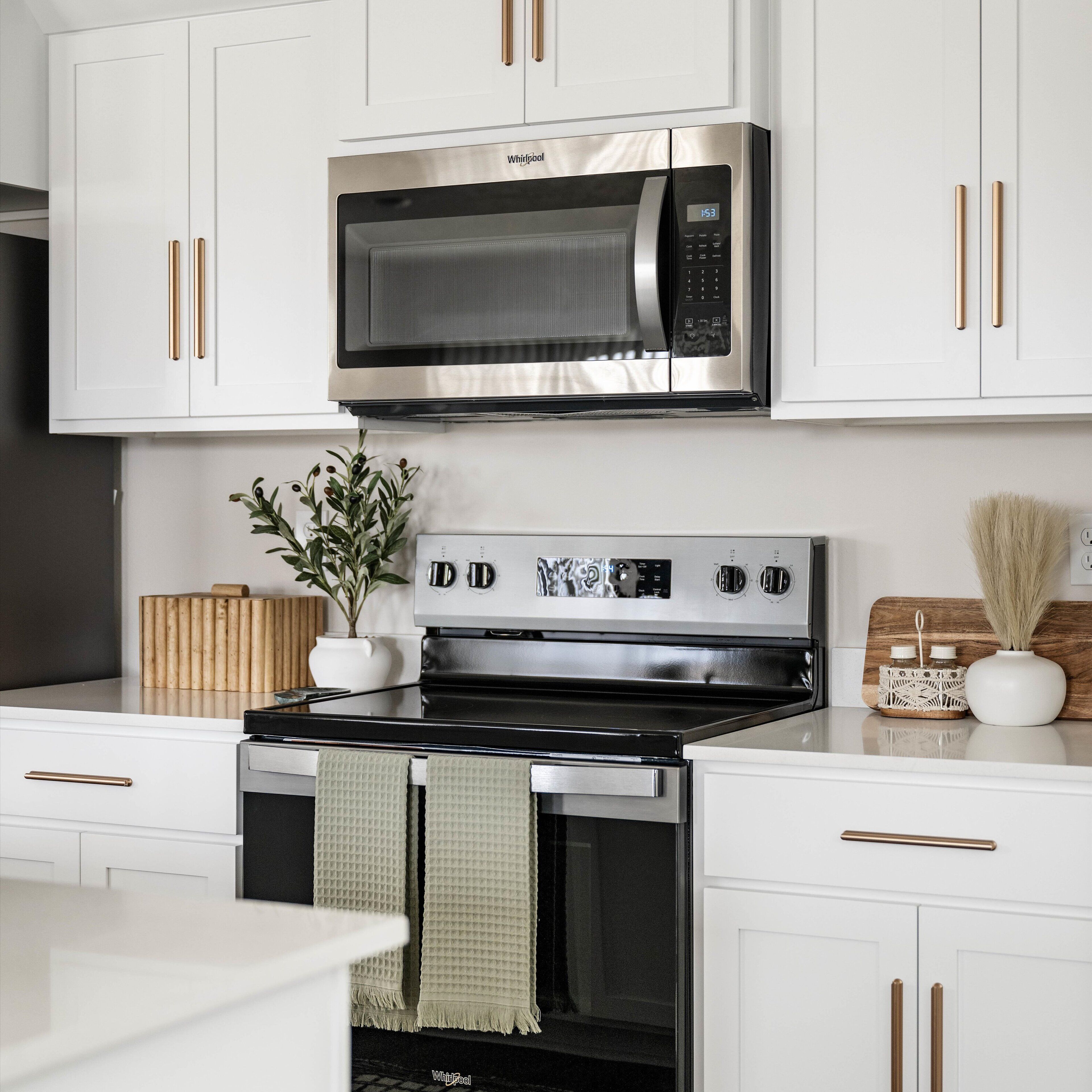A modern kitchen with white cabinets, a stainless steel microwave, and a stove.