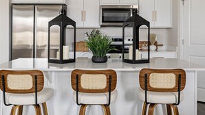 A modern kitchen with white cabinetry, a stainless steel refrigerator, a microwave, and a central island with bar stools.