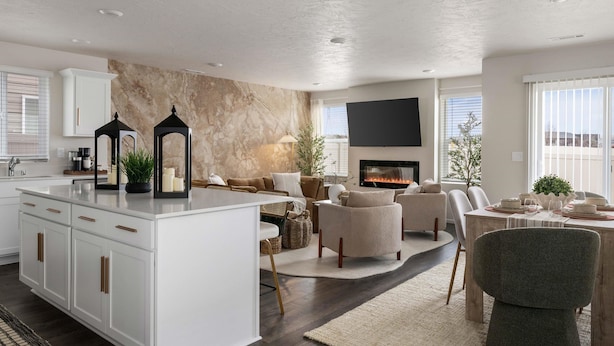 A modern living room with a fireplace, a dining area, and a kitchen with white cabinetry.