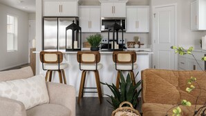 A modern kitchen with white cabinets, a central island with stools, a refrigerator, and a microwave.