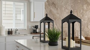 A modern kitchen with white cabinetry, a marble backsplash, and two black lanterns on the island.