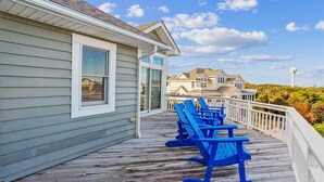 A wooden deck with blue Adirondack chairs, a white railing, and a view of houses in the background.