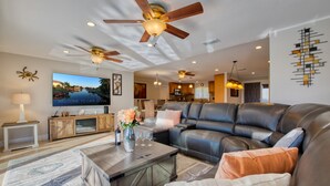 A modern living room with a leather sofa, a coffee table, and a TV displaying a scenic view. - VILLA RIVERBREEZE – HEATED POOL & SPA | GULF ACCESS | BOAT RENTAL + TOURS VOUCHER INCL. (Cape Coral)