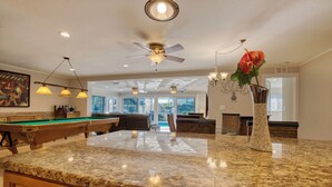 A spacious living area with a pool table, a large marble countertop, and a decorative vase with a red flower. - VILLA RIVERBREEZE – HEATED POOL & SPA | GULF ACCESS | BOAT RENTAL + TOURS VOUCHER INCL. (Cape Coral)