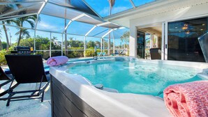 A hot tub with a glass enclosure, lounge chairs, and a patio area with palm trees. - VILLA RIVERBREEZE – HEATED POOL & SPA | GULF ACCESS | BOAT RENTAL + TOURS VOUCHER INCL. (Cape Coral)