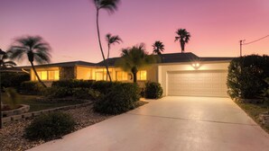 A residential house with a driveway, palm trees, and a garage. - VILLA RIVERBREEZE – HEATED POOL & SPA | GULF ACCESS | BOAT RENTAL + TOURS VOUCHER INCL. (Cape Coral)