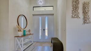 Un couloir avec une console blanche, un miroir, un banc et une porte donnant sur l’extérieur.