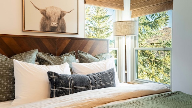 A bedroom with a bed, pillows, a framed artwork, a window with a view, and a lamp.