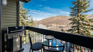 A balcony with a grill, a chair, and a table.