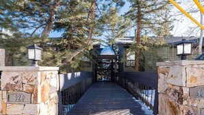 A wooden bridge with stone walls and metal railings, leading to a covered area with a snow-covered roof.