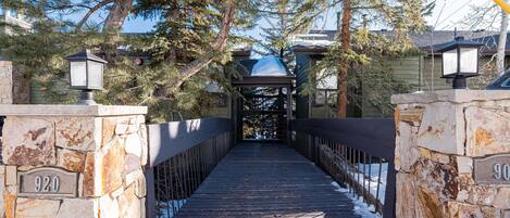 Eine Holzbrücke mit Steinwänden und Metallgeländern, die zu einem überdachten Bereich mit einem schneebedeckten Dach führt.