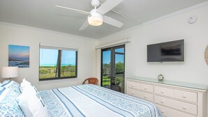 Un dormitorio con cama, televisión, ventilador de techo, ventana con vistas y cómoda.