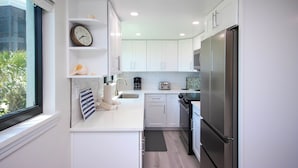 Una cocina moderna con armarios blancos, un refrigerador de acero inoxidable, una cafetera y un ventanal con vistas a la vegetación.