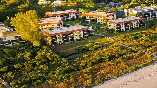 Vista aérea de um hotel à beira-mar, com vários edifícios, uma praia de areia e uma visão clara do oceano.