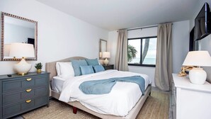 Ein modernes Hotelzimmer mit Bett, Nachttischen, einem Fernseher und Blick auf den Ozean.