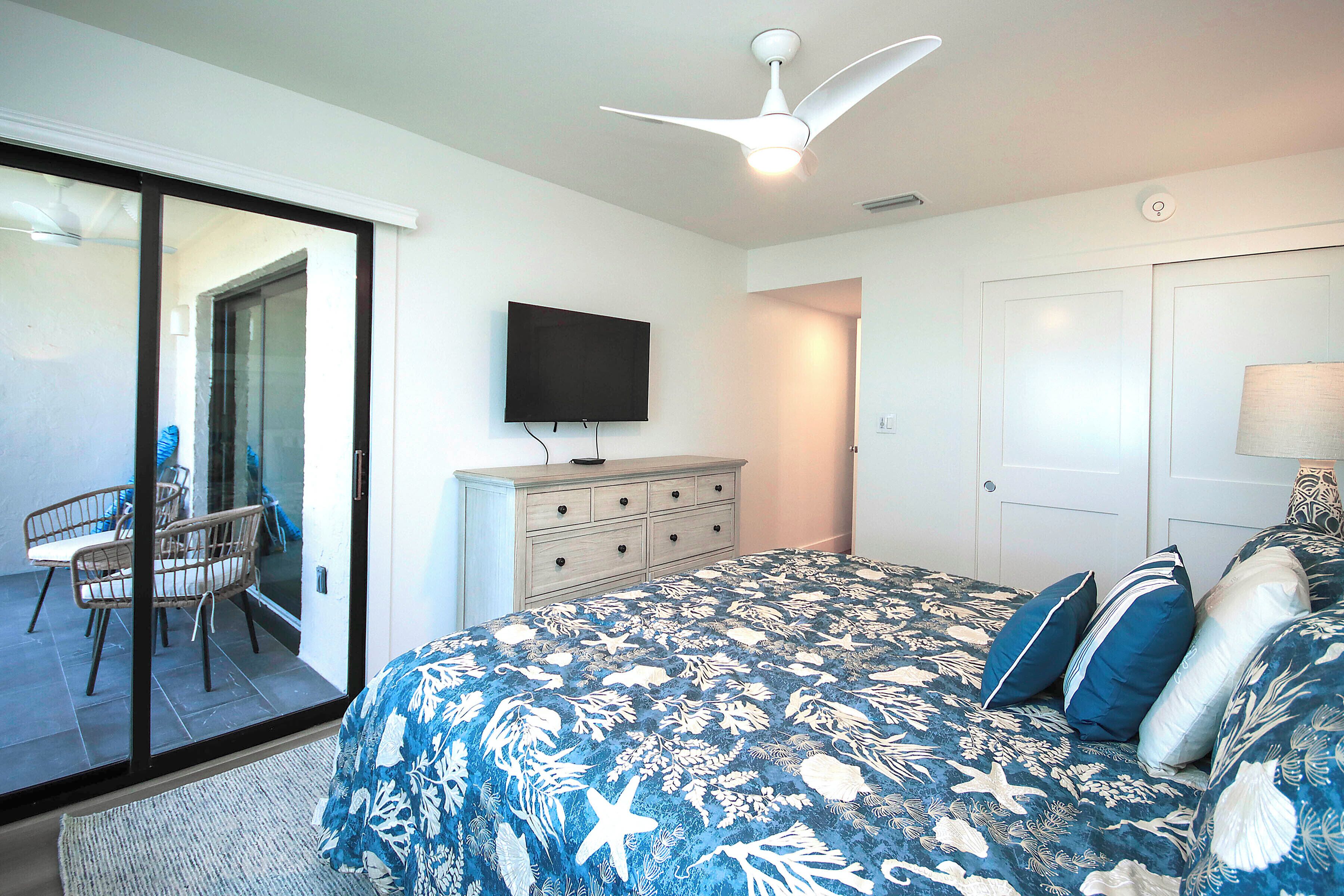 Une chambre à coucher comprenant un lit, une commode, un téléviseur et un ventilateur de plafond.