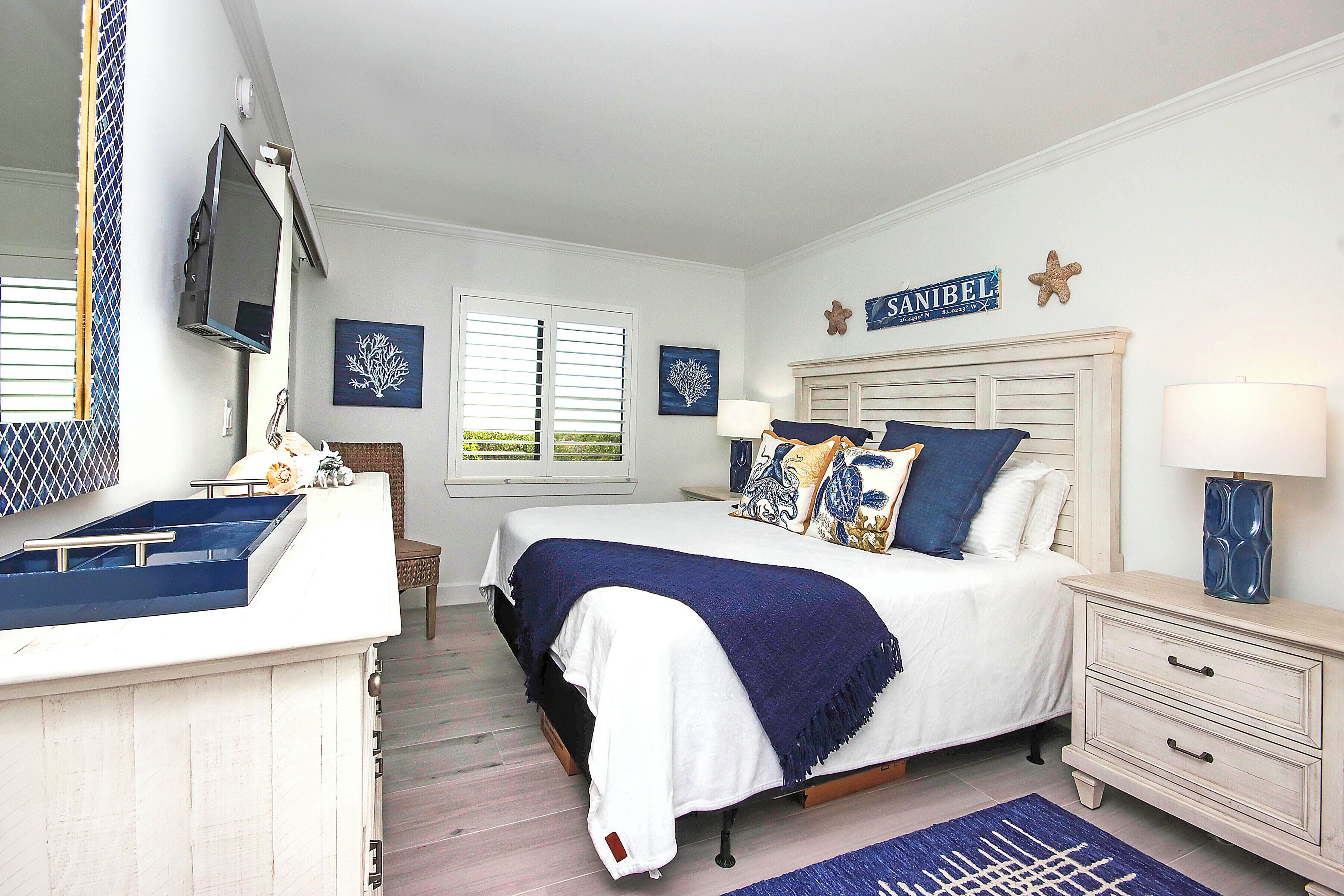 A bedroom with a bed, bedside tables, a dresser, a TV, and artwork on the walls.